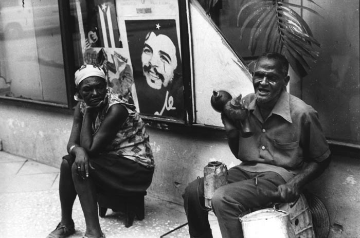 Man Making Music on Street and Woman Sitting Beside Him, Cuba